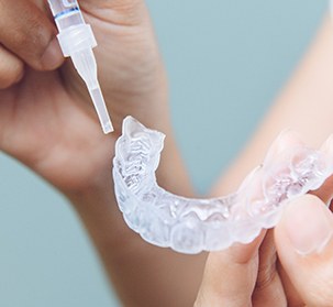 A woman placing gel on an OTC teeth whitening tray