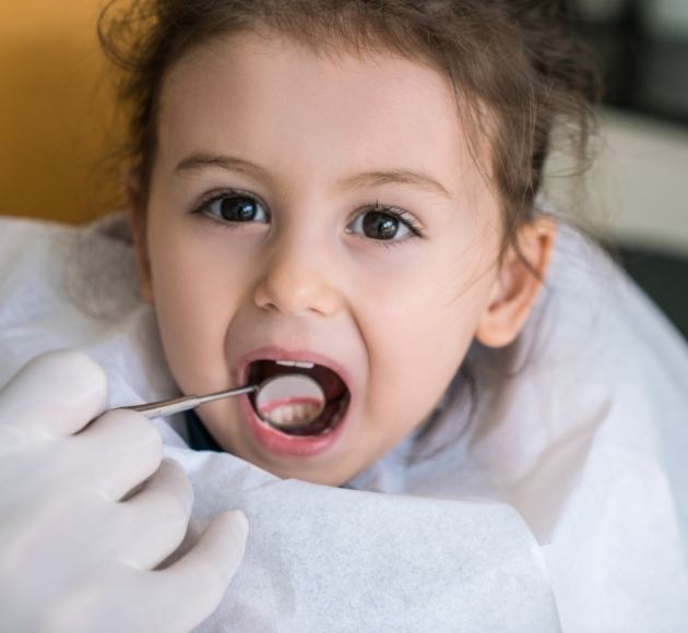 Dentist examining child's smile after tooth colored filling treatment