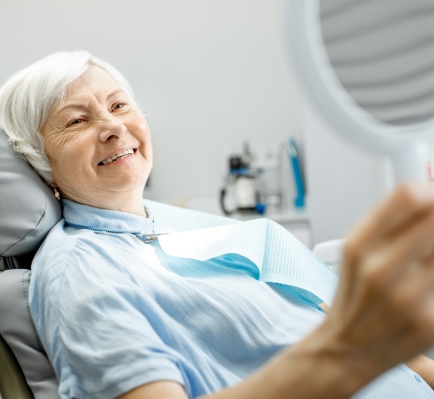 Woman looking at her smile and enjoying the benefits of dental implant retained dentures