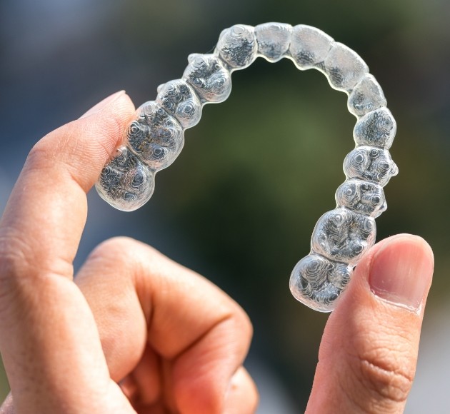 Hand holding up an Invisalign tray