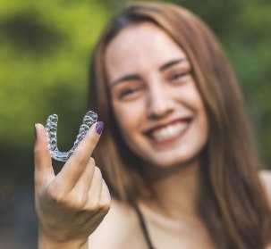 Woman holding up her Invisalign tray after replacing broken aligners