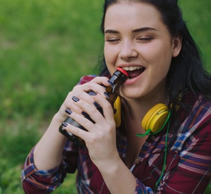 closeup of woman opening bottle with teeth 