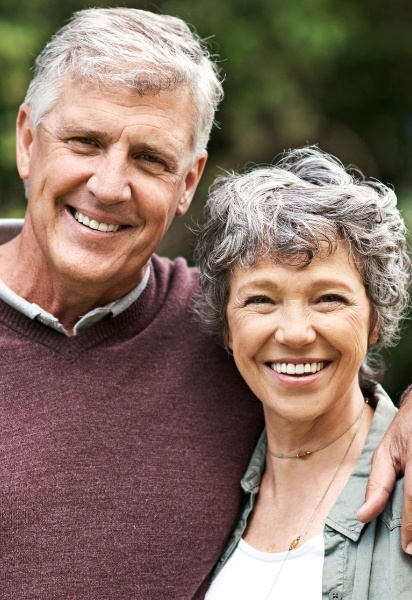 Man and woman smiling after replacing missing teeth with dental implants