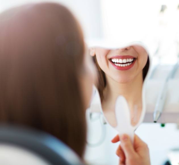 Woman looking at smile in mirror after teeth whitening