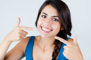A woman with both hands pointing at her smile. 