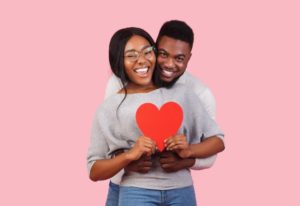 young couple on gray sweaters holding love heart